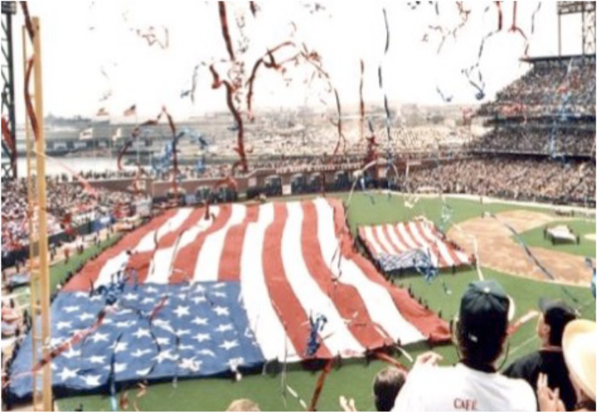 Large American flag unfurled on a stadium field during a sports event.