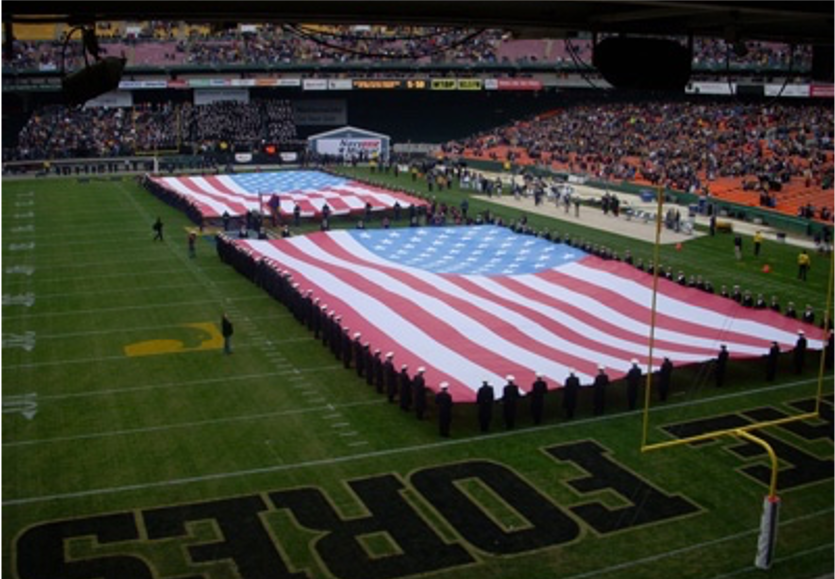 Large American flags displayed on a football field during a game.