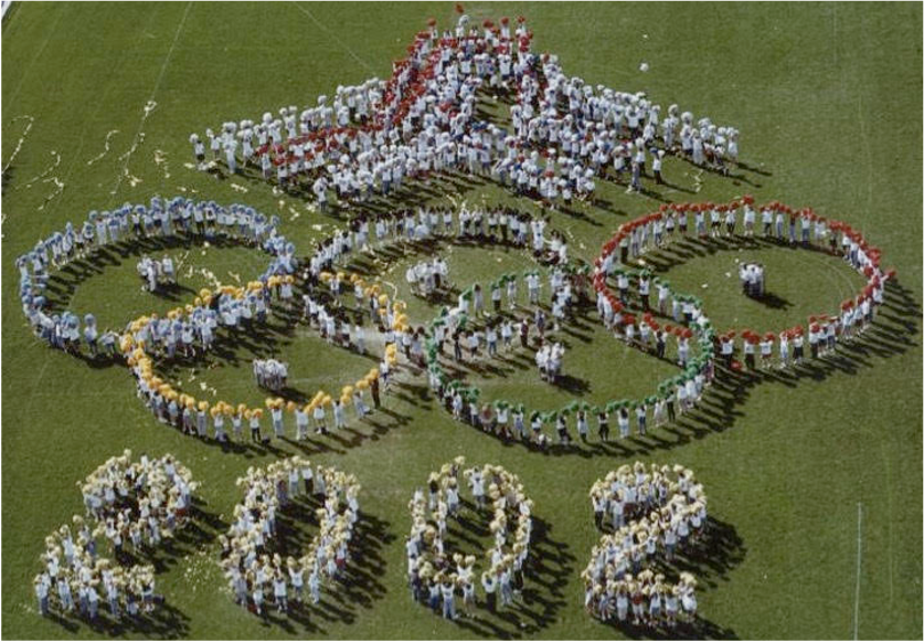 People forming the Olympic rings and Tokyo 2020 on grass.