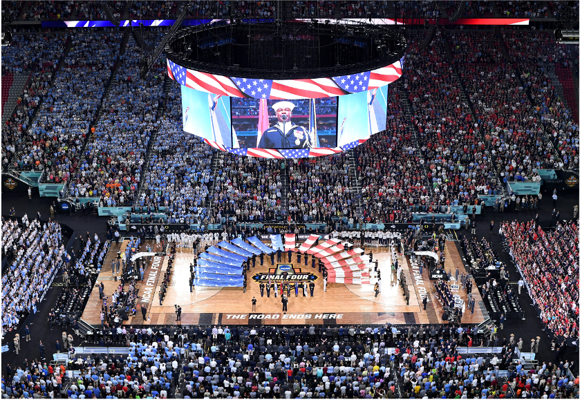 A large basketball arena filled with fans during a patriotic event.