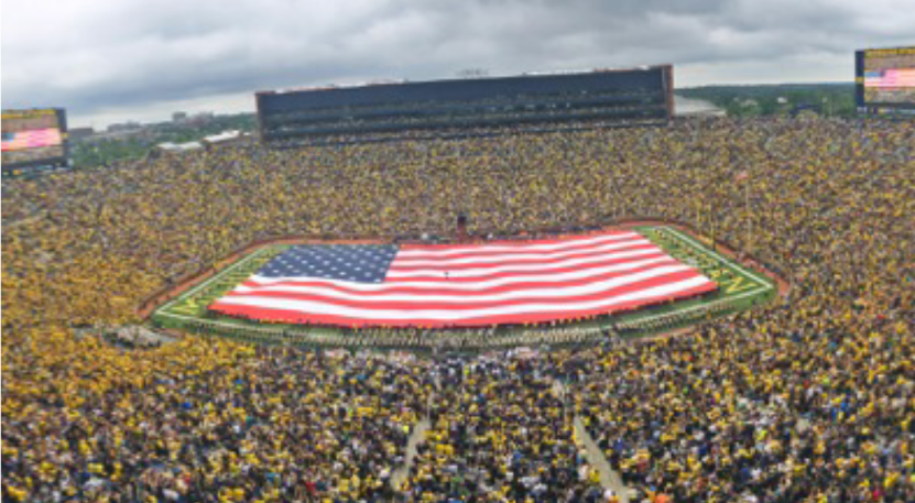 Large American flag displayed on a football field during a crowded game.
