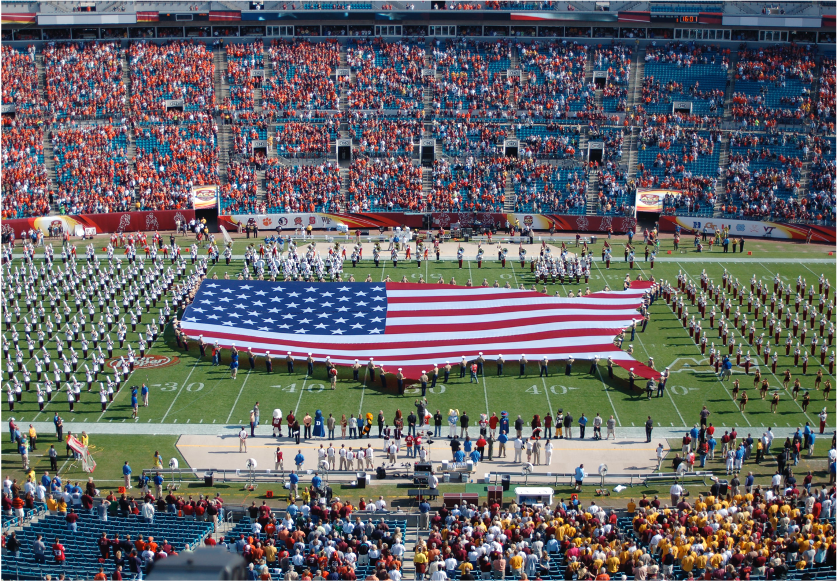 Large American flag displayed on football field during ceremony.